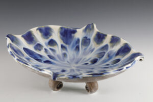 Footed bowl with blue glaze drips on a white background creating a unique effect.