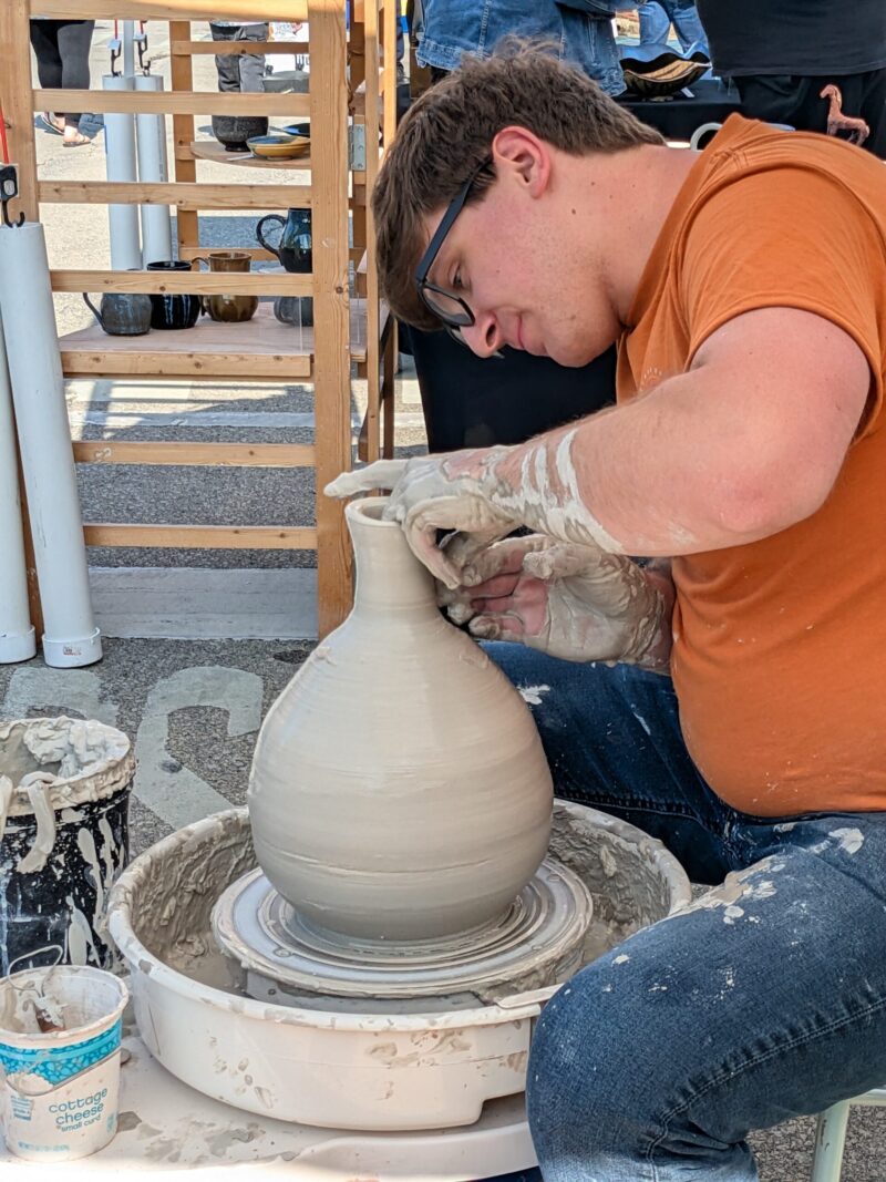 Man throwing on a pottery wheel creating a 14" tall vase