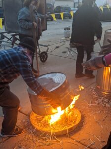 Flaming pottery is covered by a metal can to allow it to smoke and create a reduction atmosphere