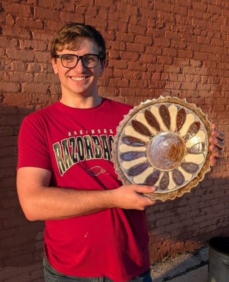 Colin Hunter holding a 14" raku plate with a flower design of copper and white crackle glaze with a scalloped edge.